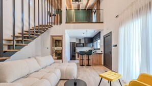 Un salon moderne avec un canapé, une table basse et un fauteuil jaune. Un escalier mène à un niveau supérieur.