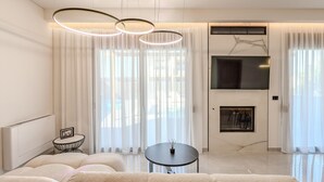 A modern living room with a sofa, a round table, and a TV mounted on the wall. - Rosy Villas Collection, for up to 20,  2 Pools & Jacuzzi (Anopolis)
