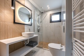 Et moderne badeværelse med en hvid vask, et stort spejl, en glasafskærmet brusekabine og et toilet.