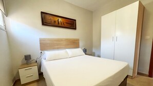 A neatly made bed with a wooden headboard, a bedside table with a lamp, and a wardrobe. - La Colina Rural House El Duque Accommodations (Córdoba)