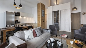 A modern living room with a sofa, coffee table, and chairs. There is a kitchen area with a refrigerator, microwave, and dining table. A fireplace is visible in the background. - Apartment in La Rosiere With Stunning Alpine Views (Montvalezan)