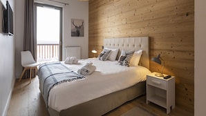 A modern bedroom with a wooden wall, a large bed with white bedding, a bedside table with a lamp, and a chair. - Apartment in La Rosiere With Stunning Alpine Views (Montvalezan)