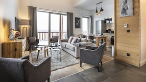 A modern living room with a sofa, chairs, a coffee table, and a dining area. There is a balcony with a view, a kitchen area, and a wooden wall with a picture. - Apartment in La Rosiere With Stunning Alpine Views (Montvalezan)