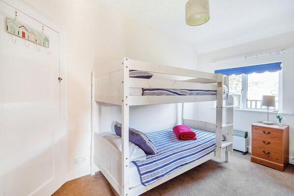 Une chambre avec un lit superposé, une fenêtre, un radiateur et une commode en bois.
