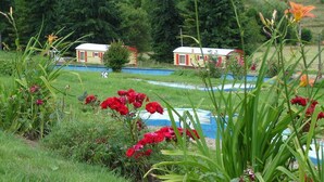 A garden with red flowers and a small pond. - Rental of comfortable trailers for 4 people at DEVALPARC leisure park (Livarot-Pays-d'Auge)