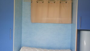 A bedroom with a bed, a blue wardrobe, and a beige curtain. - Rental of comfortable trailers for 4 people at DEVALPARC leisure park (Livarot-Pays-d'Auge)