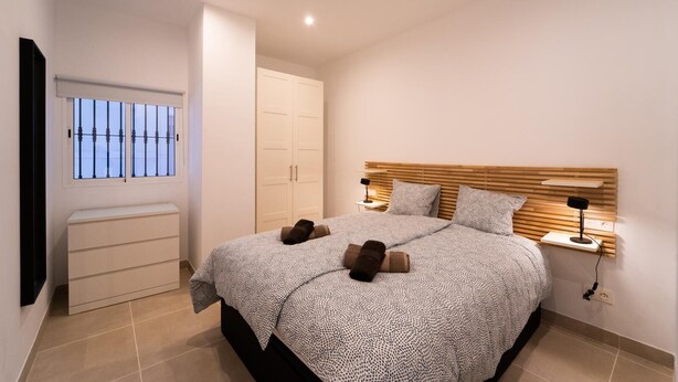 Ein Schlafzimmer mit einem Bett, Nachttischlampen, einem Kleiderschrank und einem Fenster mit Gitterstäben.