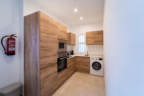 A compact kitchen with wooden cabinetry, a built-in oven, a microwave, a coffee maker, and a washing machine.