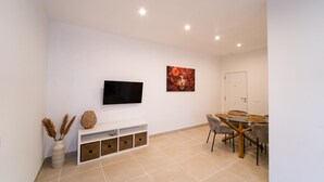 Ein modernes Wohnzimmer mit Flachbildfernseher, einem Esstisch mit Stühlen, einem weißen Konsolentisch und einem großen Gemälde.