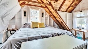 Een slaapkamer met een schuine kap, een bed, een klein tafeltje en een raam.