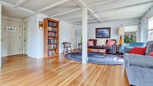 Een ruime woonkamer met houten vloeren, een boekenkast, een bank en een salontafel.