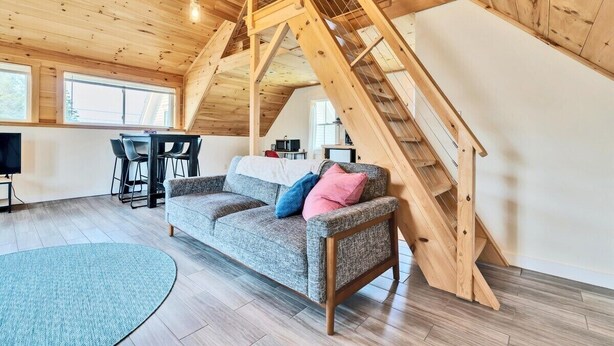 Een kamer in loftstijl met een houten trap, een bank en een eethoek.