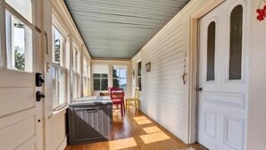 A covered porch with a wooden floor, white exterior walls, and a door on the right. - Seaside Farmhouse | Cozy Waterfront Getaway in Ten (Saint George)