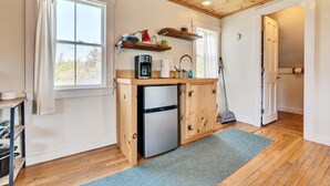 Una cocina compacta con refrigerador, armarios de madera, cafetera y escoba.