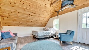 Un dormitorio estilo loft con techo inclinado, una cama, un sillón azul y un ventanal grande.