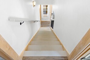A staircase with wooden steps and white walls, leading to a room with a wooden floor and a window.