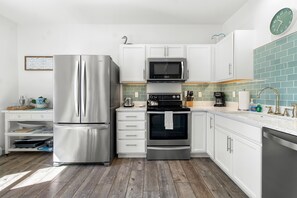 A modern kitchen with stainless steel appliances, white cabinetry, and a green tiled backsplash.