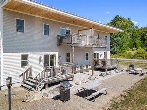 Een gebouw met twee verdiepingen, een balkon, terrasmeubels en een barbecue.
