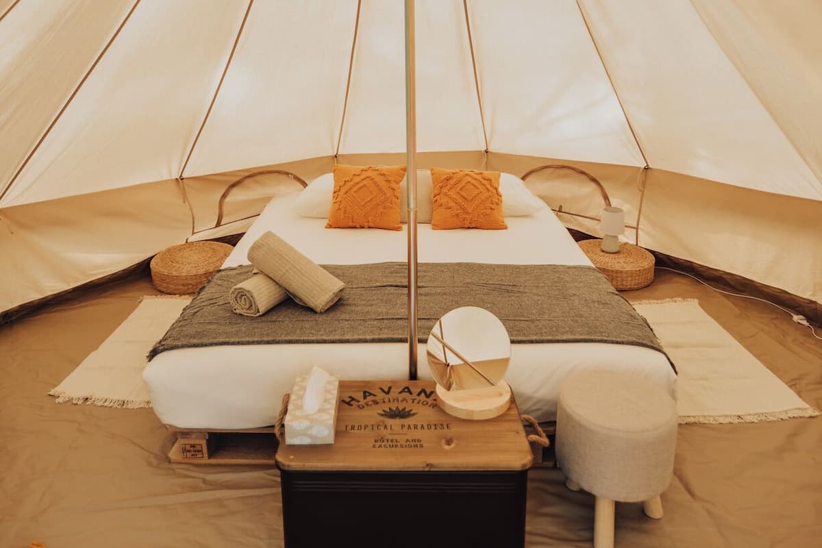 A tented accommodation with a central bed, pillows, a small table, and a woven mat.