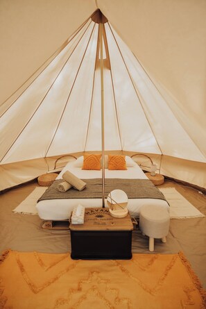 A tented accommodation with a central bed, pillows, a small table, and a woven mat.