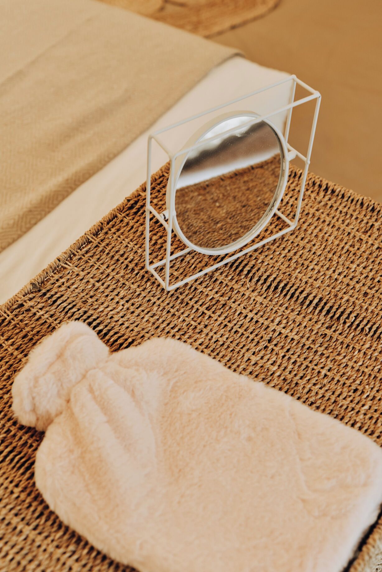A woven mat, a white towel, and a clear glass container on a bed.