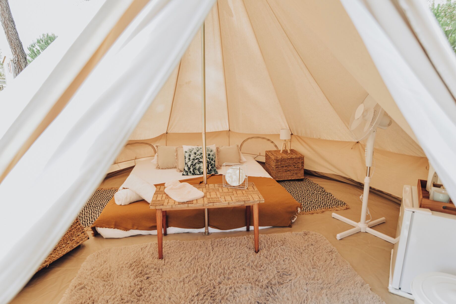 Ein gemütliches Zelt mit Bett, einem kleinen Tisch und einem Ventilator.
