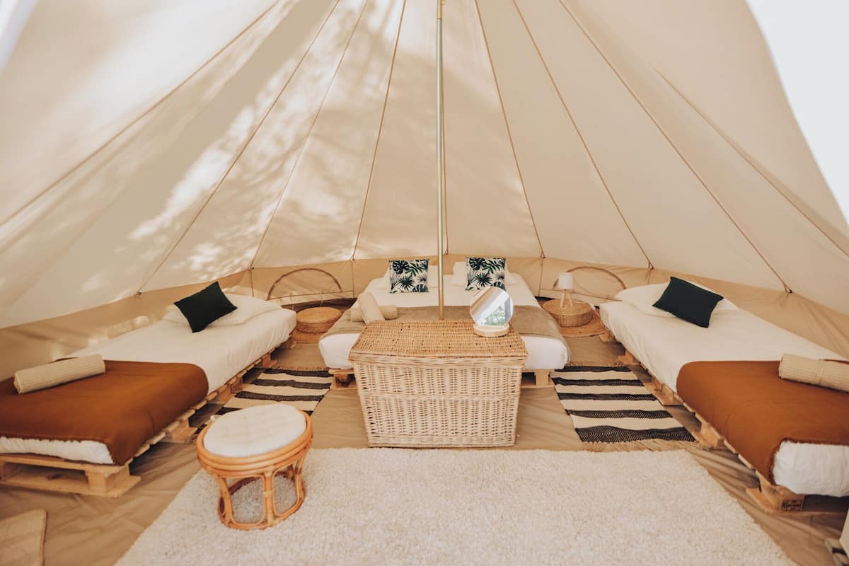 A cozy tent with two beds, a central seating area, and a small stool.