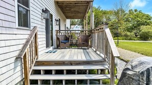Une terrasse en bois avec une rambarde, deux chaises en osier et une table.