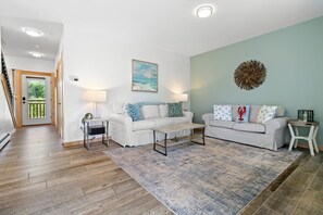 A living room with two white sofas, a coffee table, a rug, and a wall art piece.