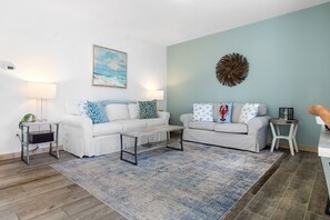 Ein Wohnzimmer mit zwei weißen Sofas, einem Couchtisch, einem Teppich und einer Wanddekoration.