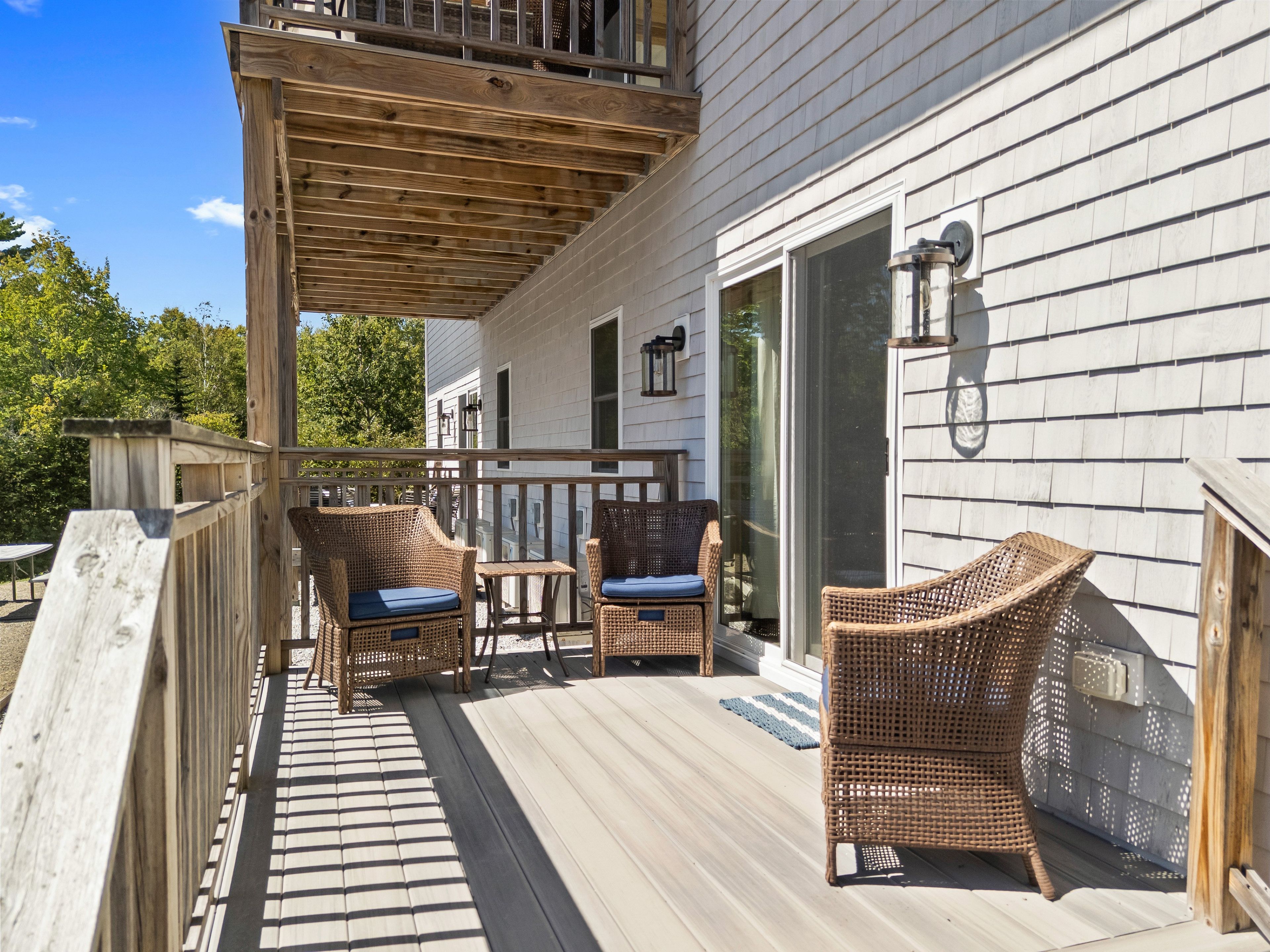 A wooden deck with wicker furniture and a glass door leading to a covered area.