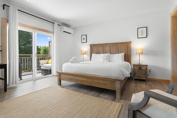 A bedroom with a wooden bed, two bedside tables, a large window with a view of greenery, and a balcony.