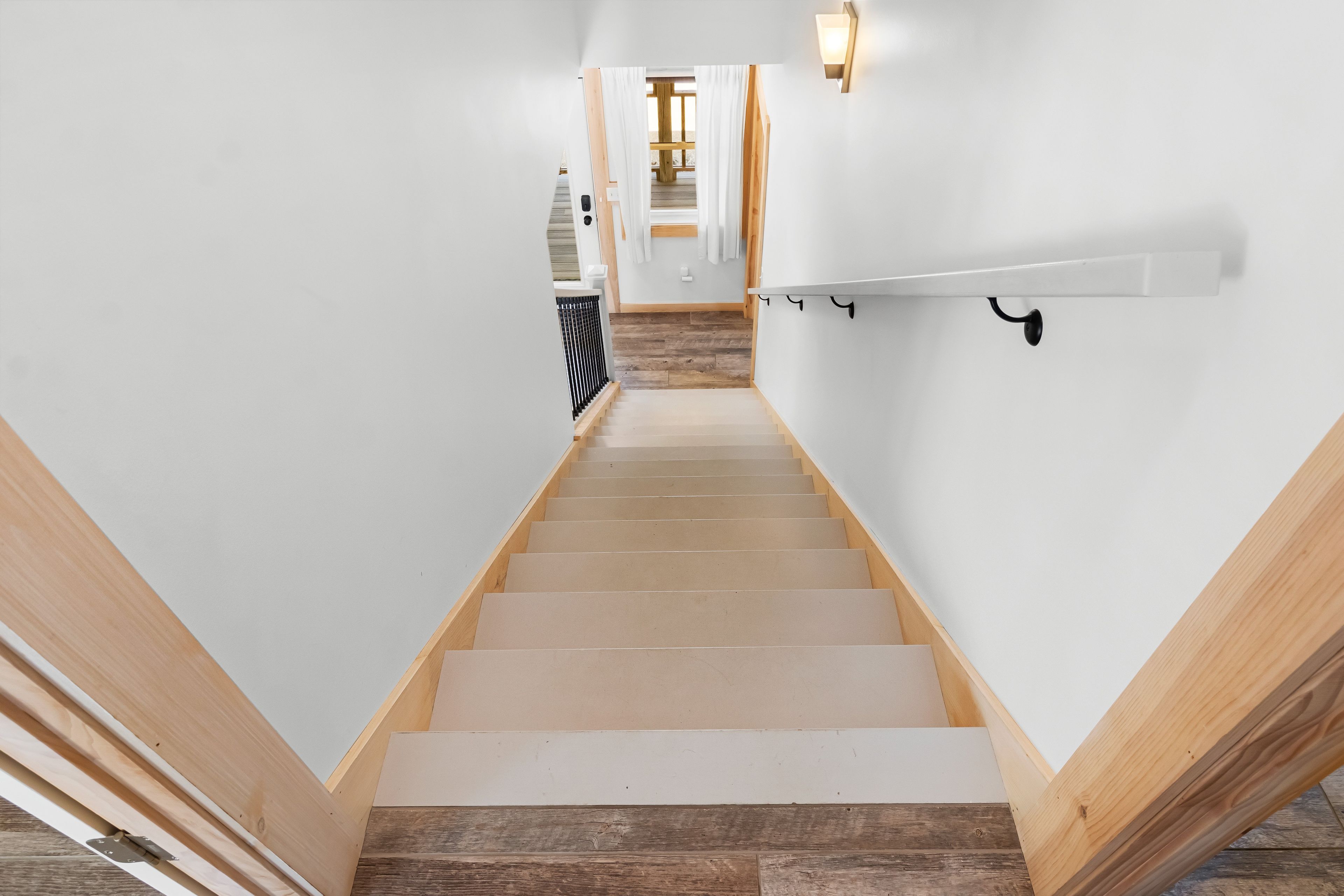 Una escalera con escalones de madera y paredes blancas que conduce a una habitación con piso de madera.