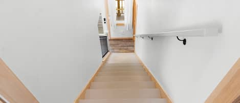 Una escalera con escalones de madera y paredes blancas que conduce a una habitación con piso de madera.