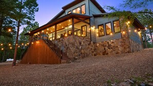 Una casa de dos pisos con base de piedra, fachada de madera y un porche delantero cubierto con luces colgantes.