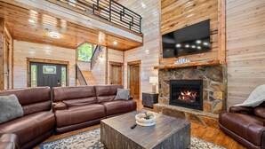 Amplia sala de estar con un sofá de cuero color café, chimenea de piedra y techo de madera.