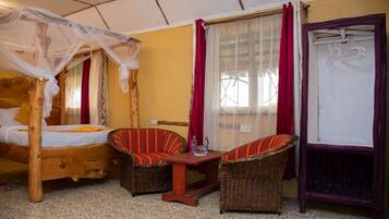 Una habitación con una cama, dos sillas de mimbre, una mesita y una ventana con cortinas.