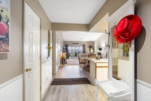 A hallway with a white door, a dining area with a table and chairs, and a bathroom with a sink and mirror.