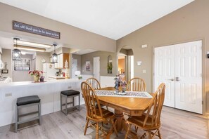 A dining area with a wooden table and chairs, a kitchen area with a white countertop, and a white door.