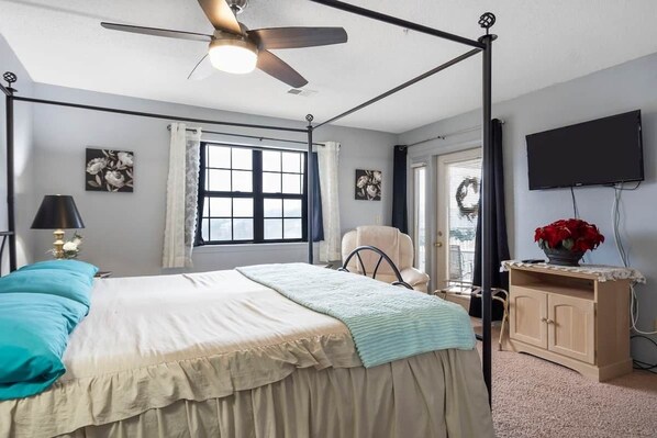 A bedroom with a bed, a ceiling fan, a window with curtains, a television, and a cabinet with a flower vase.