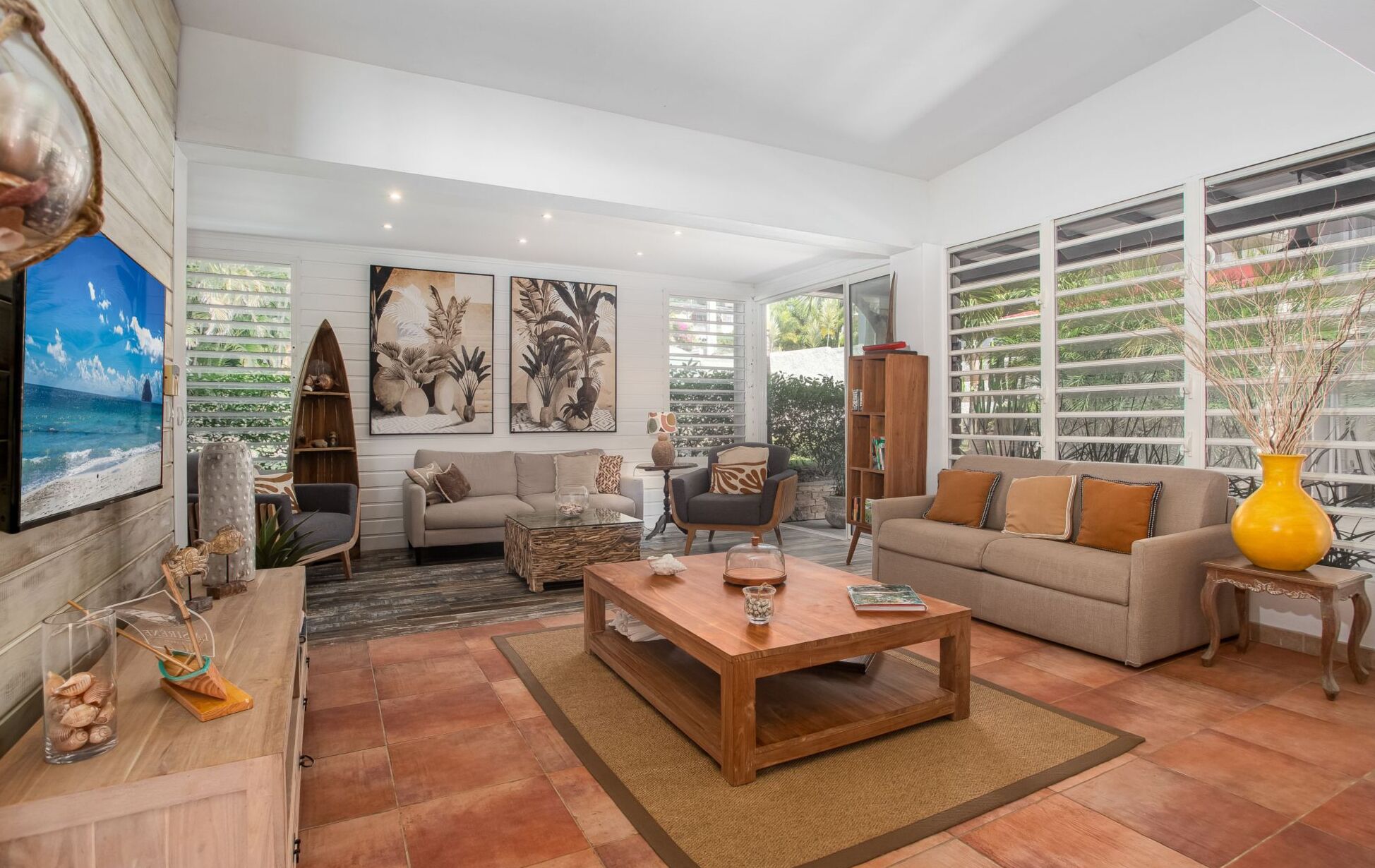 A spacious living room with a large TV, comfortable seating, and a view of greenery through large windows.