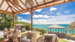 A covered outdoor seating area with wicker furniture and a view of the ocean. - La Sirène du Diamant  (Le Diamant)