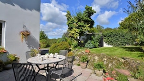 A patio with a round table and chairs, surrounded by potted plants and a garden. - Thatched Cottage - Sleeps 6 With Countryside Views (Dorchester)