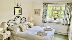 A neatly made bed with pillows and folded towels, a bedside table with a lamp, a framed picture on the wall, and a window with curtains. - Thatched Cottage - Sleeps 6 With Countryside Views (Dorchester)