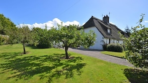 A white house with a black roof, surrounded by a well-maintained lawn and trees. - Thatched Cottage - Sleeps 6 With Countryside Views (Dorchester)