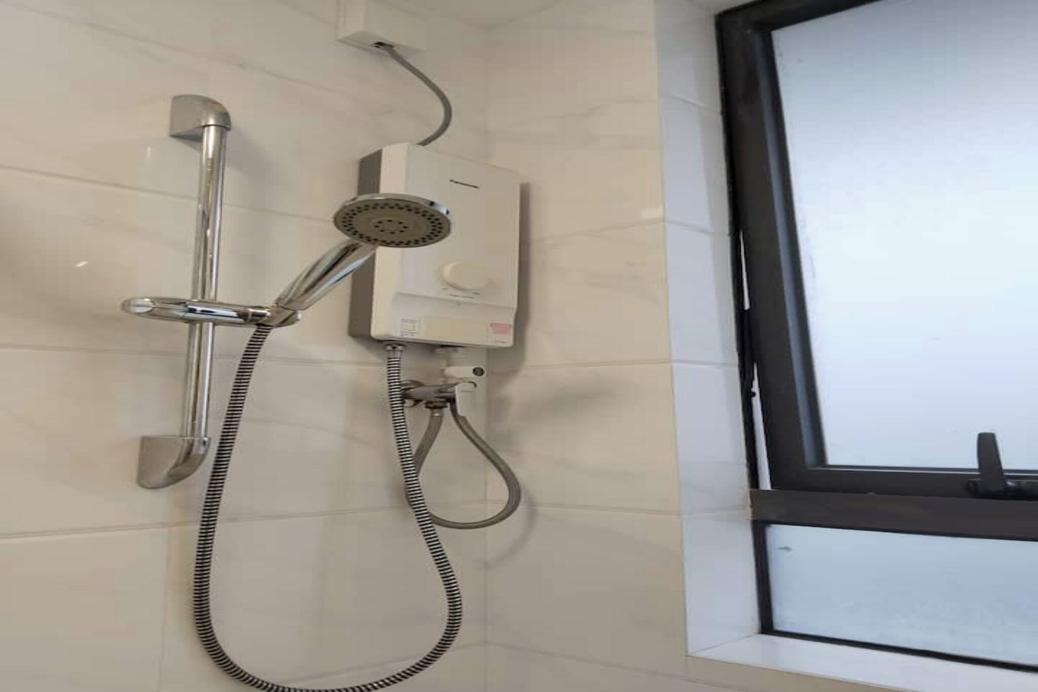 Een douche met een handdouche en een douchekop, aangesloten op een bedieningspaneel dat aan de muur is bevestigd.
