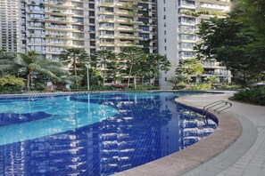 A swimming pool with tiled edges, surrounded by greenery and tall residential buildings in the background.