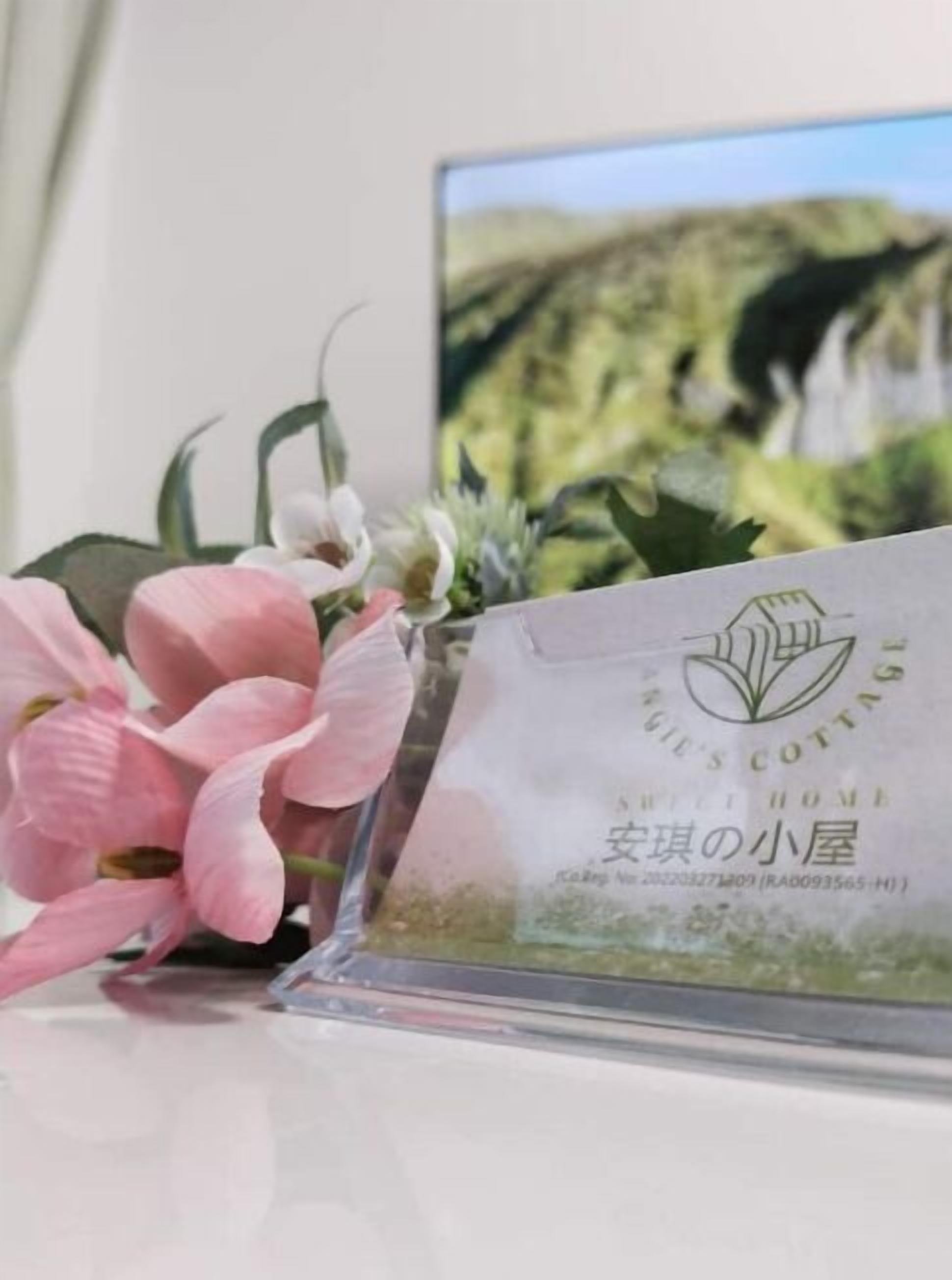 Une photographie encadrée représentant un paysage naturel avec une maison, une orchidée rose et un panneau transparent en plastique portant un texte et un logo.