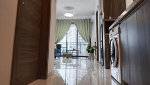 A modern hallway with a washing machine, a dining area with a table and chairs, and a view of a cityscape through large windows. - Holiday Home@Forest City~TV Box~2BR1B 4-6pax 1807 (Gelang Patah)
