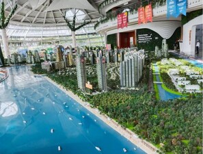 Un atrio interior con techo de cristal, una fuente central y una maqueta de zona residencial con vegetación y edificios.